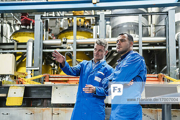 Confident male technicians in blue coat discussing while standing in industry