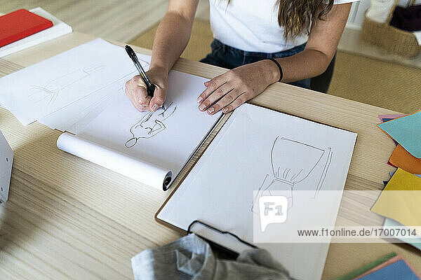 Junge Modedesignerin beim Skizzieren eines Entwurfs in einem Buch im Atelier