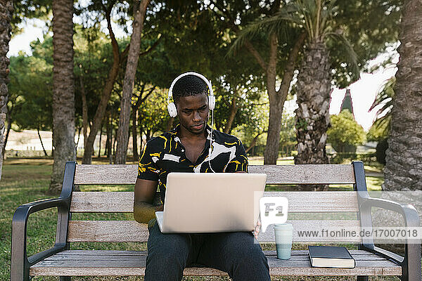 Geschäftsmann  der mit Kopfhörern im Park an einem Laptop arbeitet