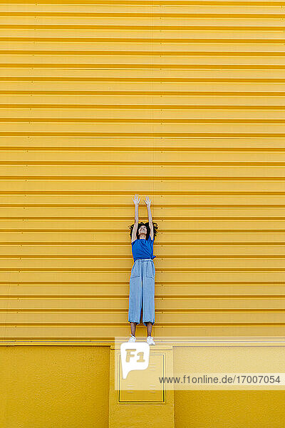 Lächelnde Frau  die sich an der gelben Wand hochzieht  auf dem Bahnsteig stehend
