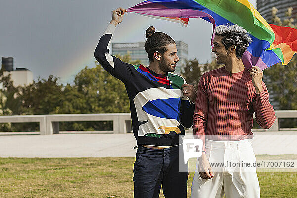 Smiling affectionate man with rainbow scarf looking at male partner in park