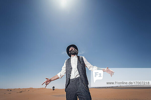Man with a beard and hat screaming in the dunes of the desert of Morocco