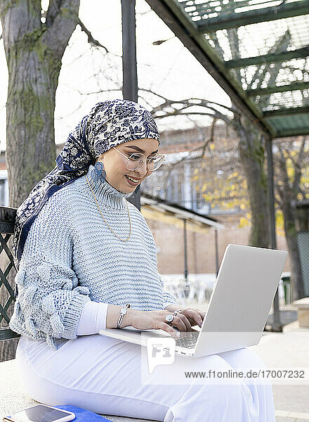 Junge Frau lächelt bei der Arbeit am Laptop im Freien