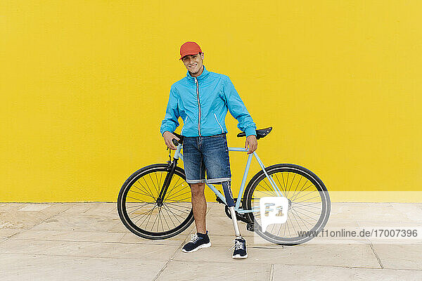Men wearing cap holding bicycle while standing against yellow wall