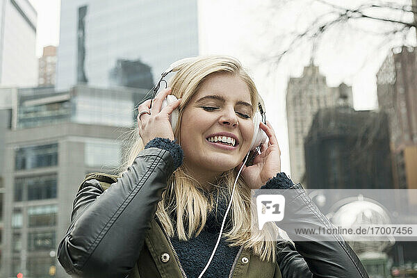 Junge Frau lächelt beim Musikhören in der Stadt