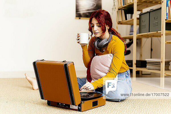 Young woman drinking coffee while using turntable at home