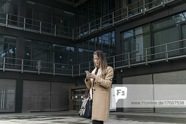 Unternehmerin mit Smartphone vor Bürogebäude