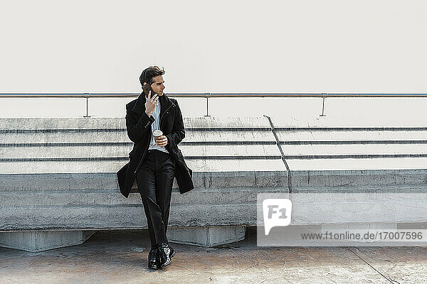 Businessman with takeaway coffee on cell phone outdoors