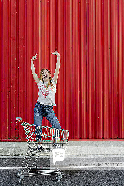 Girl rocking in a shopping cart in front of red wall