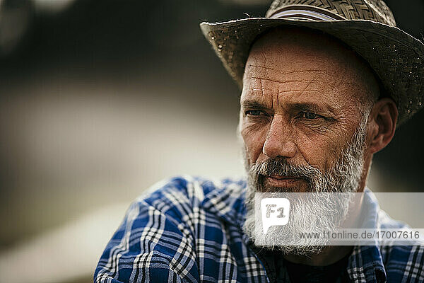 Älterer Landwirt mit Hut  der im Freien steht und wegschaut