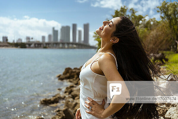 Schöne Frau mit geschlossenen Augen genießt sonnigen Tag an der Bucht in der Stadt