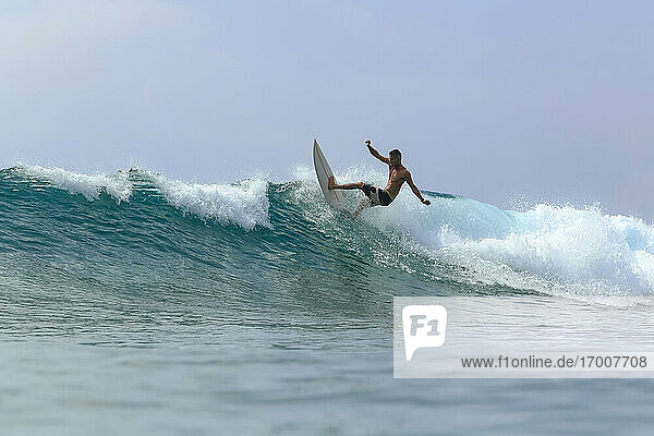 Mann mit Surfbrett surft auf Welle gegen klaren Himmel