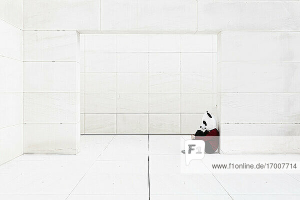 Depressive Frau mit Panda-Maske sitzt an der Tür vor einer weißen Wand
