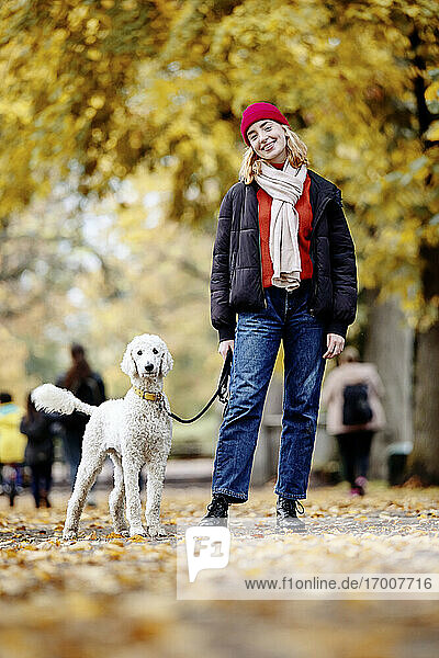 Lächelndes Teenager-Mädchen mit Hund auf der Straße im Park