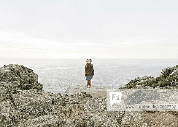 Frau mit Kamera auf einem Felsen stehend  Blick auf das Meer  Rückansicht