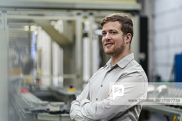 Confident businessman with arms crossed standing in manufacturing industry