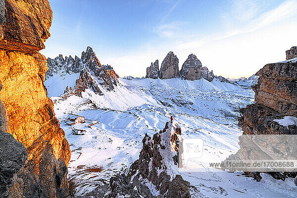 Mann auf Felsen bewundert den verschneiten Monte Paterno und die Drei Zinnen bei Sonnenuntergang  Sextner Dolomiten  Südtirol  Italien  Europa