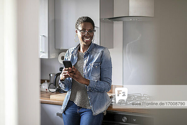 Smiling woman with smart phone in kitchen