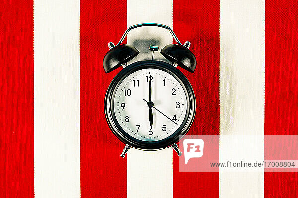 Alarm clock lying on white and red striped pattern