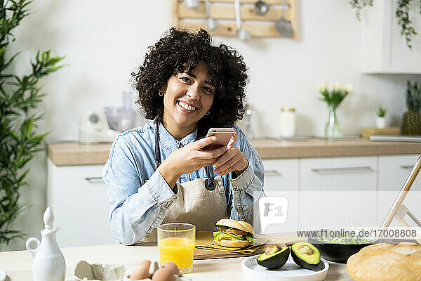 Porträt einer jungen Frau  die ein Smartphone am Küchentisch benutzt