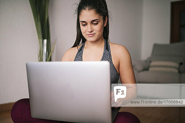 Junge Frau benutzt einen Laptop  während sie zu Hause im Wohnzimmer sitzt