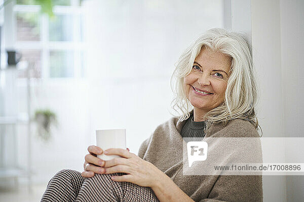 Happy senior woman holding coffee cup while sitting in living room at home