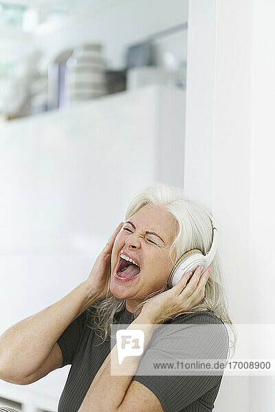 Fröhliche Frau genießt Musik über Kopfhörer  während sie in der Wohnung schreit