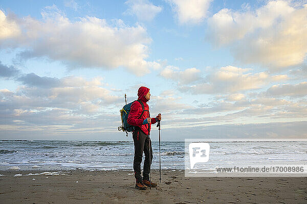 Man with backpack and hiking poles standing at beach  Mediterranean Sea  Italy