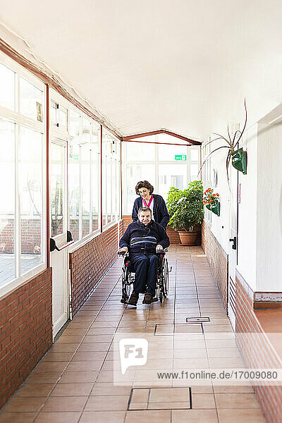 Weibliche Krankenschwester hilft behindertem Mann im Rollstuhl sitzend auf dem Flur eines Pflegeheims