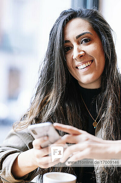 Glückliche Frau mit Kaffeetasse und Smartphone in einem Cafe