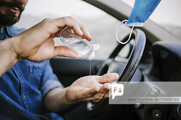 Junger Mann benutzt Handdesinfektionsmittel im Auto während COVID-19