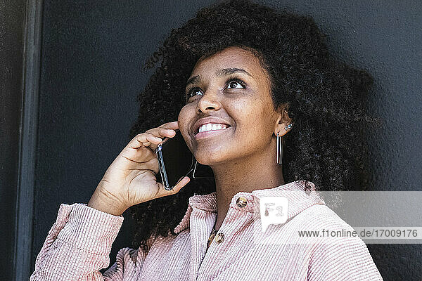 Junge Afro-Frau telefoniert und schaut weg gegen eine schwarze Wand