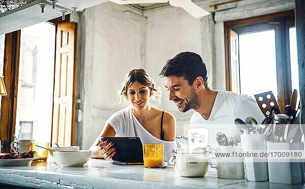Junges Paar schaut beim Frühstück zu Hause auf ein Tablet