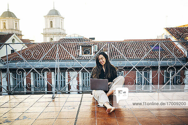 Junge Frau  die einen Laptop benutzt  während sie auf einer Terrasse gegen den klaren Himmel sitzt
