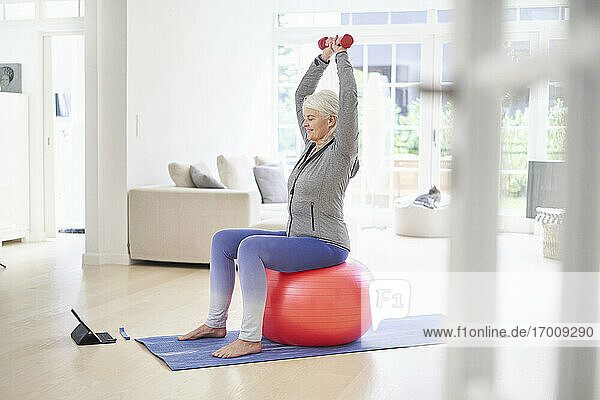Retired woman exercising while learning from online tutorial through digital tablet at home