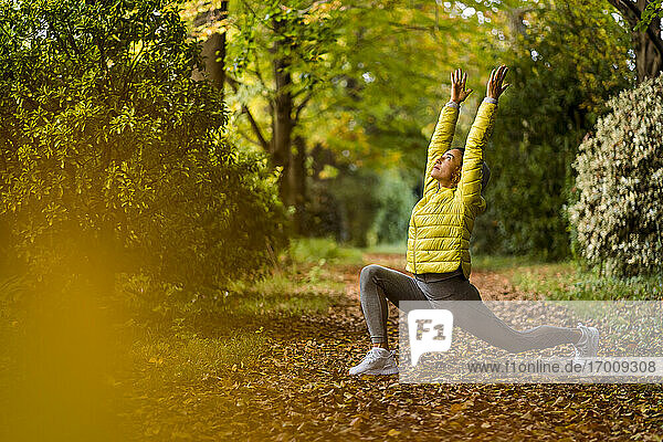 Sportler mit erhobener Hand beim Yoga  während er auf einem Fußweg im Park trainiert