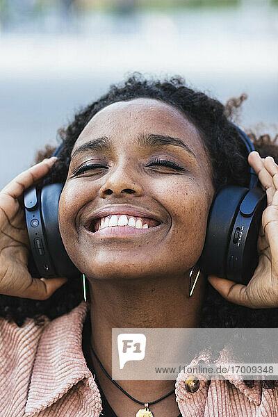 Glückliche Afro-Frau mit geschlossenen Augen hört Musik über Kopfhörer in der Stadt