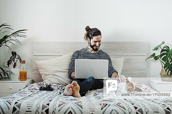 Lächelnder Mann  der mit seinem Hund spielt  während er einen Laptop zu Hause benutzt