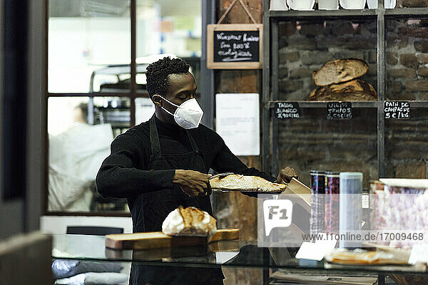 Männlicher Bäckereibesitzer verpackt Brot in eine Papiertüte  während er in der Bäckerei steht