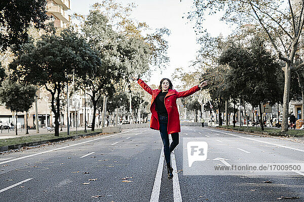 Unbekümmerte Frau in roter Jacke tanzt und springt auf der Straße