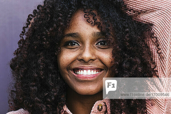 Glückliche afro-junge Frau mit lockigem Haar an der Wand