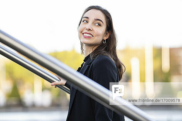 Young businesswoman smiling while standing by railing