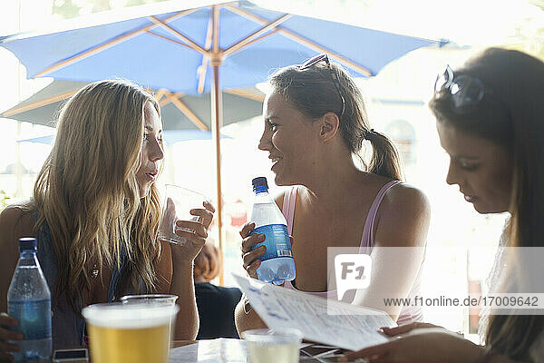 Junge Frauen unterhalten sich  während ihr Freund im Strandrestaurant die Speisekarte liest