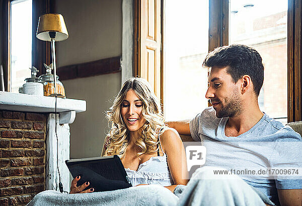Young couple cuddling on couch at home watching tablet