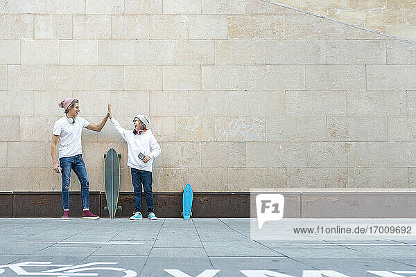Young man and boy giving high-five while standing by skateboards against wall