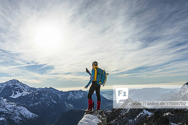 Älterer männlicher Wanderer  der sein Smartphone benutzt  während er auf dem Gipfel eines Berges steht  Orobic-Alpen  Lecco  Italien
