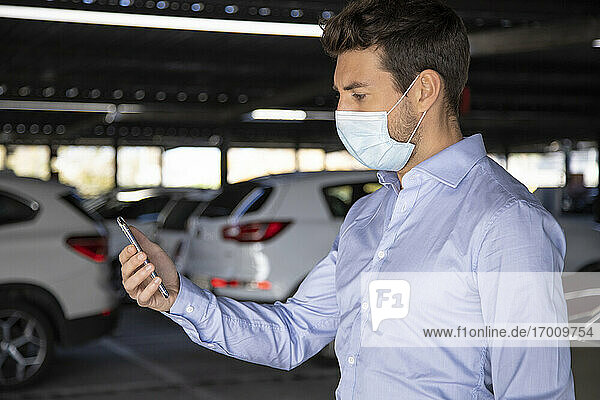 Male entrepreneur using mobile phone in parking lot during pandemic