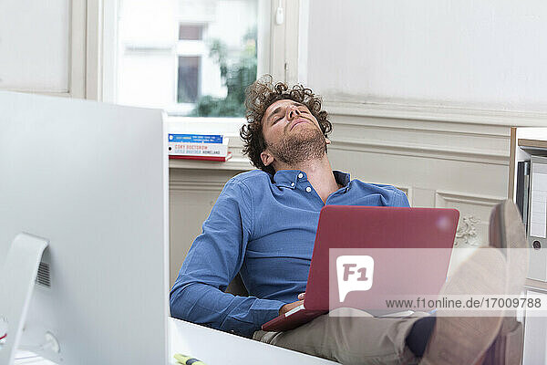 Young businessman sleeping with laptop in office cabin