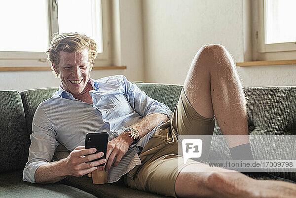 Glücklicher Mann  der ein Mobiltelefon benutzt  während er zu Hause sitzt