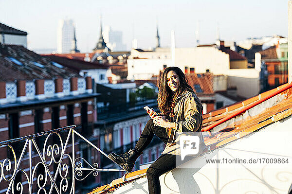 Glückliche junge Frau mit Mobiltelefon auf dem Dach an einem sonnigen Tag